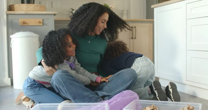 African American mother in green, two girls climbing lap hugging playing reaching bins in kitchen