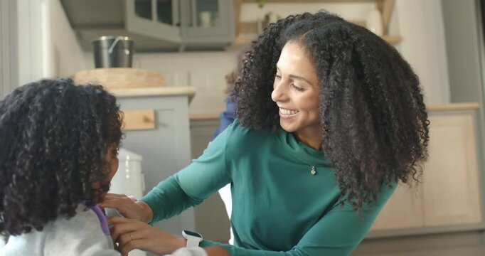 African American mother turning as younger child reaching for hug, fixing hoodie in kitchen