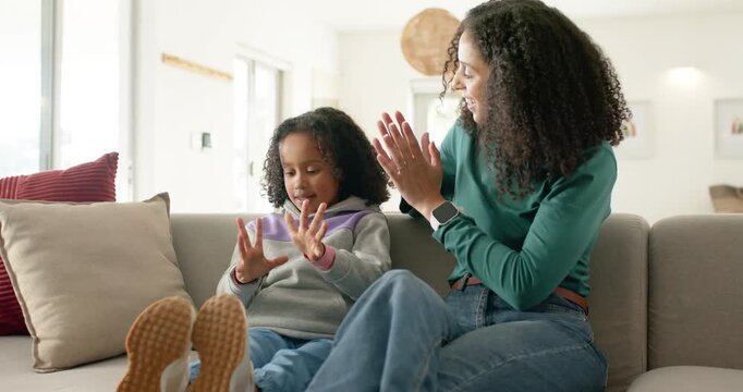African American mother guiding child holding fingers on sofa at home, child counting and smiling