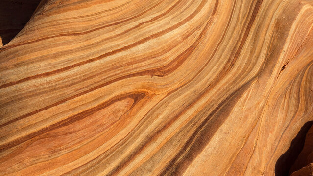 Golden sandstone rock texture with natural wavy orange and brown geological layers.