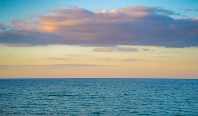 Fototapeta premium Calm blue ocean surface meeting the horizon under a serene sunset sky with soft pastel clouds, evoking peacefulness, minimalist beauty, and solitude.