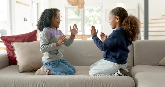 African American youth girls kneeling on couch at home raising palms clapping, high-fiving