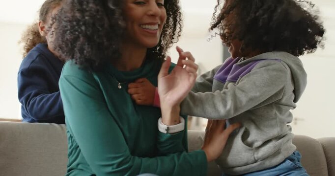 African American mom with two daughters climbing onto couch and tickling necklace while playing
