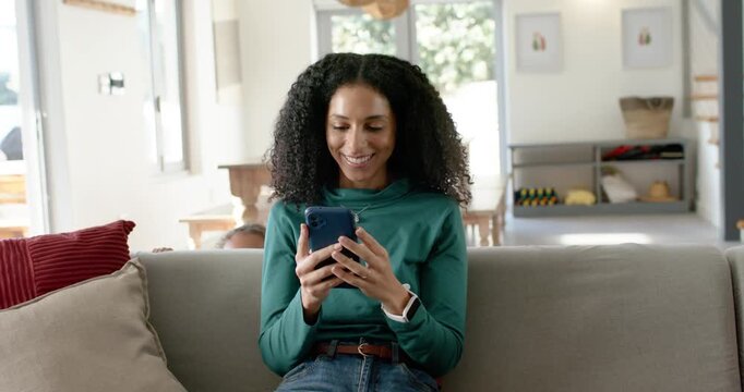 African American mom scrolling blue phone at home, youth girls peeking behind, making her laugh