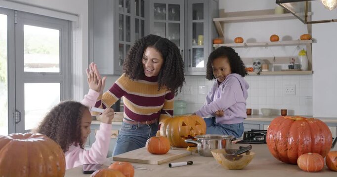African American family carving and decorating pumpkins at kitchen island starting craft, laughing