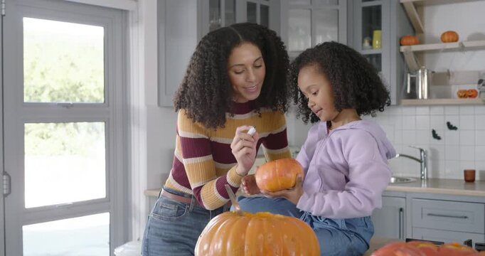 African American mother teaching daughter pumpkin decorating in kitchen, guiding hand using marker