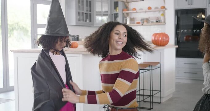 African American mom adjusting two girls' witch capes passing pumpkin buckets in kitchen for treats