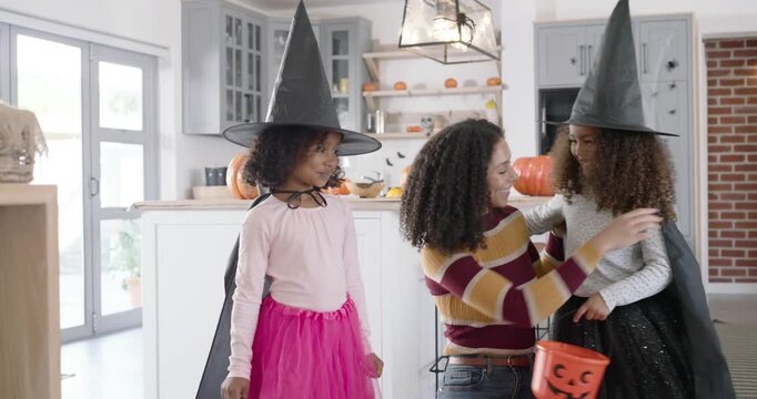 African American family prepping for Halloween, mother adjusting witch hats capes at kitchen island