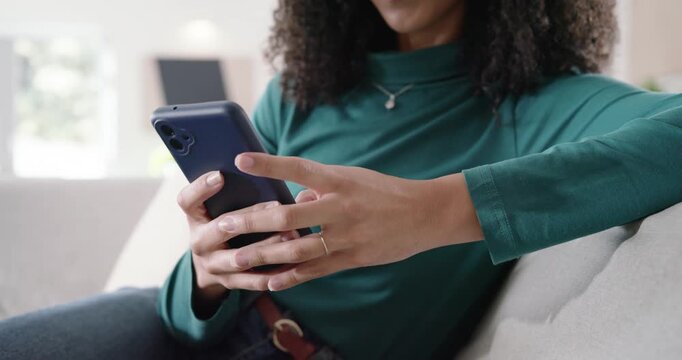 African American woman raising left hand, reaching for phone, reading, tapping, swiping on sofa