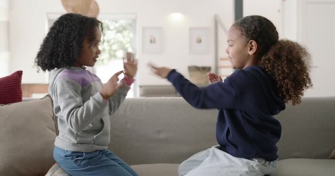 African American teenage females on sofa, raising palms, playing hand claps, speeding to high-five