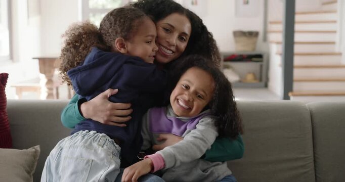 African American mother and school-age daughters climbing into lap, hugging, comforting on sofa