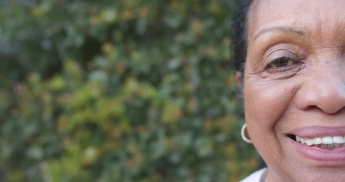Senior African American woman smiling laughing to offframe remark by hedge, hoop earring