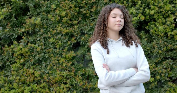 African American teen in hoodie standing at green hedge during camera reframing smiling copy space
