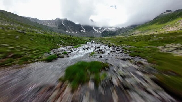 Fast aerial tracking shot over stream in green valley