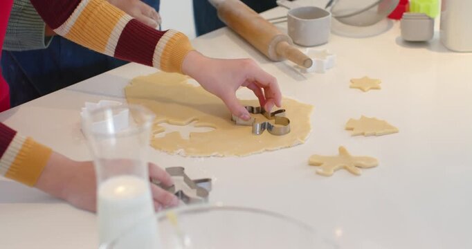 Adult and child hands reaching, pressing cutters into dough on counter, cutting cookies for baking