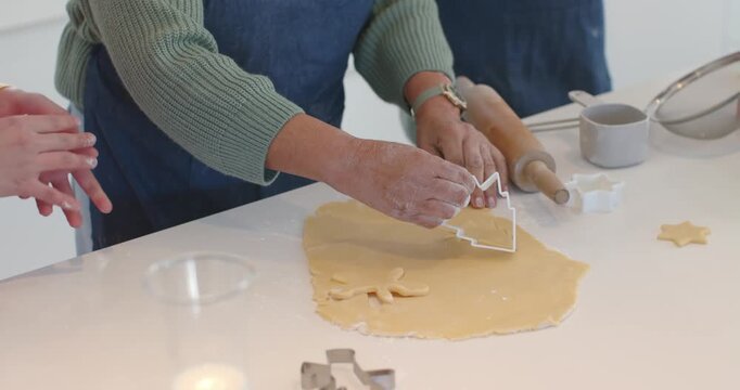 Baker is pressing tree cutter into rolled dough on counter after positioning, teaching child helper