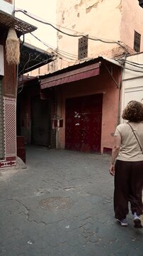 Marrakech, morocco. August 10, 2026. Caucasian woman with curly hair walking down a narrow, ancient street in the old medina of marrakech, morocco, with traditional architecture