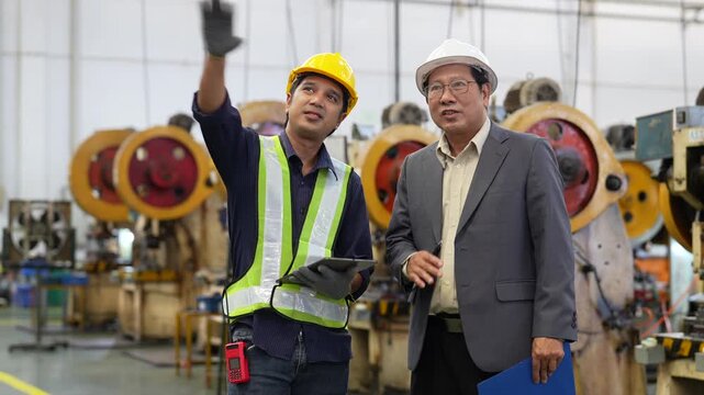 Construction worker, executive, engineer, and manager wearing hard hat and safety vest inside industrial factory, reviewing machinery during workplace inspection, collaborative teamwork