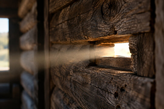 Close-up of a narrow arrow slit in a wooden wall, a single beam of light shining through, detailed wood.