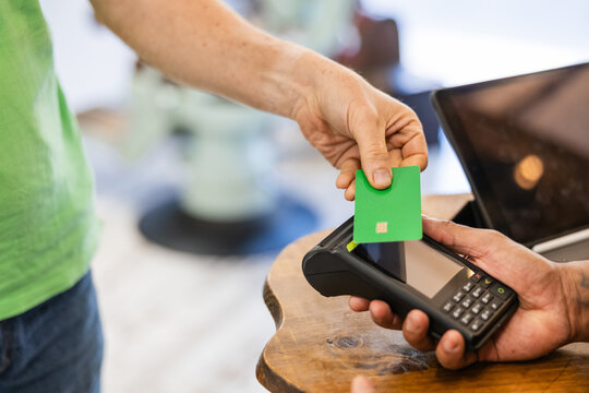 Customer making contactless payment with credit card in barbershop