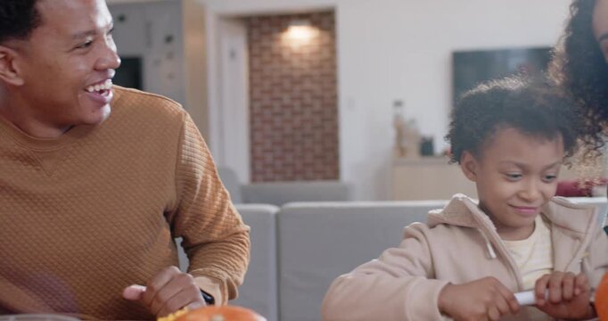 African American family parents offering white marker, guiding youth girl drawing pumpkin at table