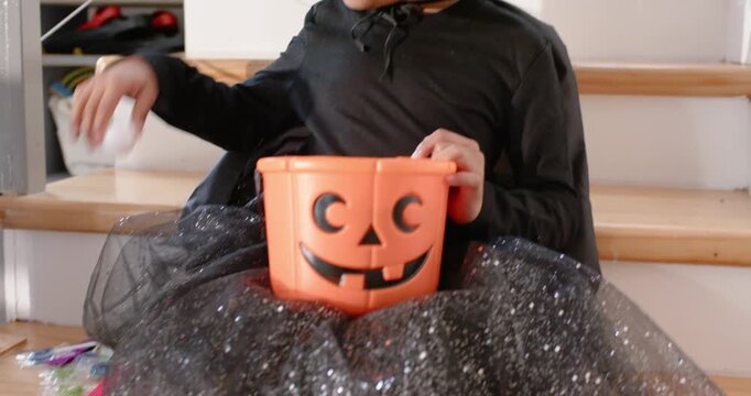 Girl child with witch hat on stairs hands resting on pumpkin-bucket and reaching treats