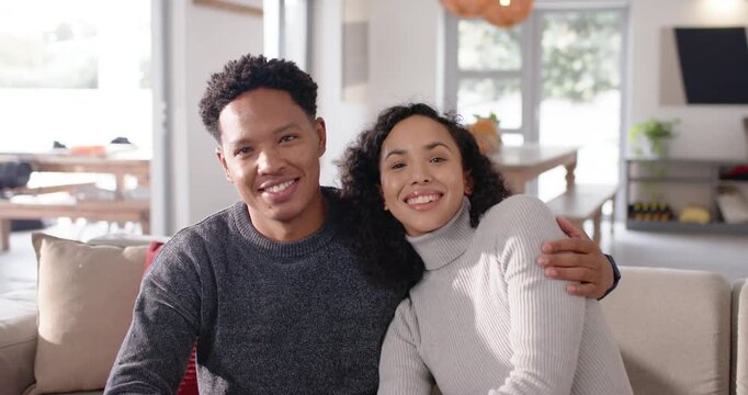 African American couple smiling at camera for portrait, nesting closer on beige sofa in living room