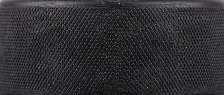 Close up texture of black rubber hockey puck edge. Diamond knurling grip pattern on sports equipment background