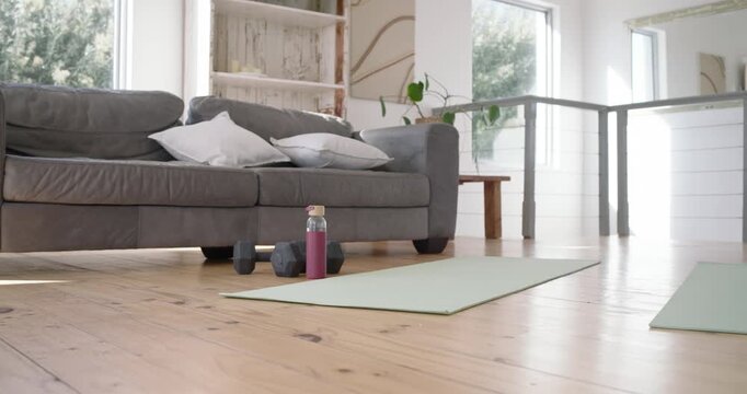 Camera is panning across two green mats in living room, weights by mats for two-person workout