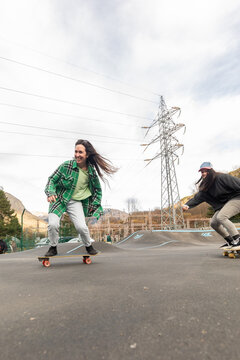 Friends skateboard at an outdoor pump track beneath power lines