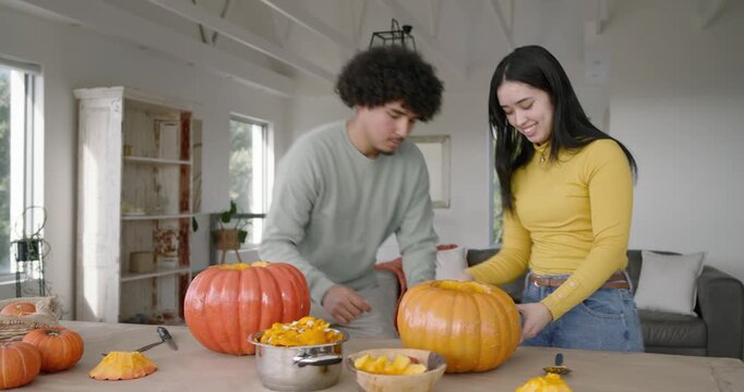 African American couple carving pumpkins, cutting lids at home, woman steadying, man scooping pulp
