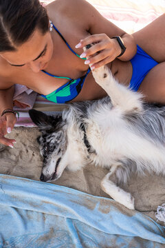 Woman relaxes with dog on beach during summer