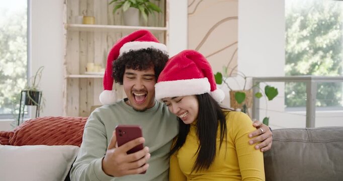 African American couple in red Santa hats on sofa, man tapping phone, woman reacting to screen