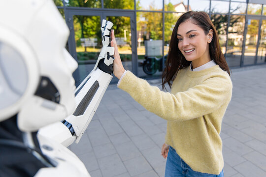 Smiling woman giving high five to futuristic humanoid robot