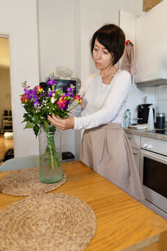 Woman arrange colorful flower bouquet in home kitchen