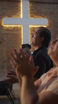 Diverse group of worshippers singing and clapping together during evangelical gathering with illuminated church cross in background expressing faith hope and spiritual unity