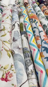 diagonal rows of printed fabric rolls on retail display, foreground ends facing camera while perspective shifts with smooth forward movement under warm lights fabric