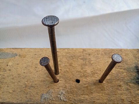 Iron nails driven into old wooden plank, high angle close-up of carpentry detail and construction concept.