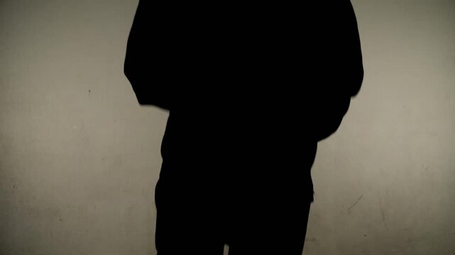 A close-up of an anonymous silhouette of a man's torso running against a wall towards the camera
