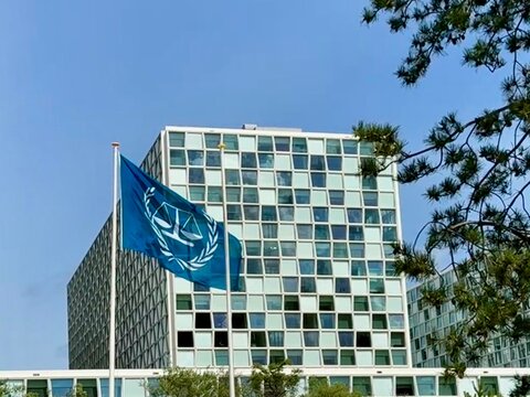 The Hague, Netherlands - June 11 2026: Blue flag of the International Criminal Court flying on a pole in front of its modern headquarters building under a clear blue sky.