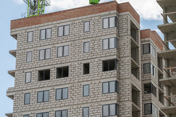 Construction is in progress on a modern building with large windows and stone-like exterior in a bustling urban area © beholdereye