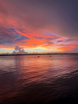 Vibrant sunset paints the sky with fiery orange and purple hues over a calm lake with kayakers
