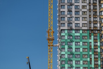 Construction workers diligently operate a tall crane shaping a vibrant new building against a clear blue sky © beholdereye