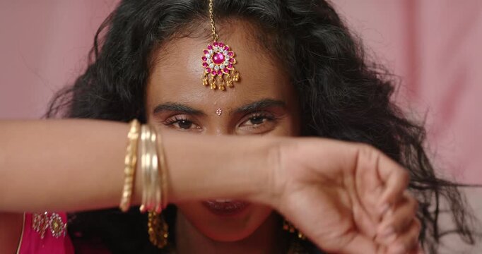 Indian woman reacting to camera, smiling, lifting arm, peeking through gold bangles at studio