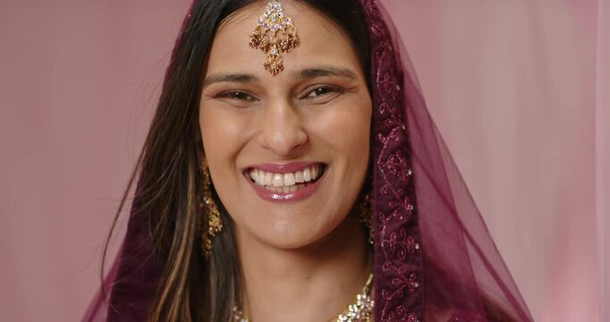 Veiled Indian woman smile turning into laugh, sliding behind curtain in studio wearing maang tikka