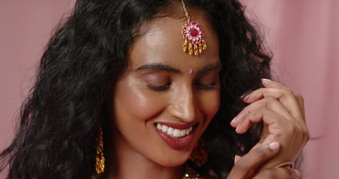 Adult Indian woman wearing pink sari posing for camera smiling brushing hair adjusting gold bangles