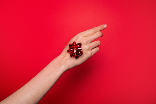 Hand holding red gift bow on vibrant red background