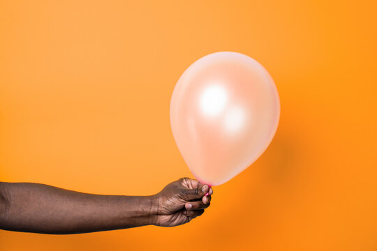 Hand holding translucent balloon against orange background