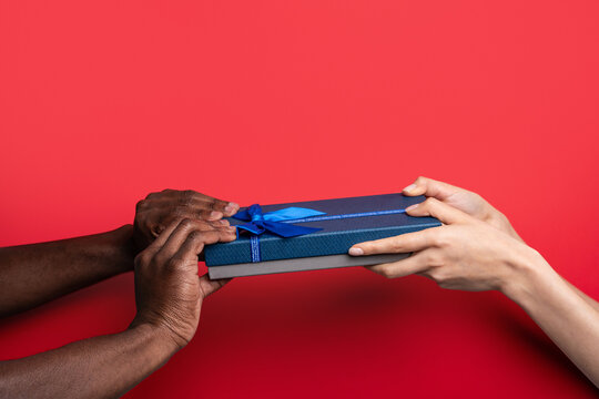 Multiethnic hands exchange blue gift box on red background