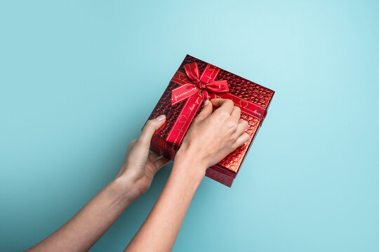Hands holding red gift box with ribbon on blue background